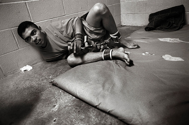 Voices From Juvenile Detention: Kids Behind Bars It sounds harmless: “pre-trial detention.” But the reality is far different. In a squat block building in Laredo, Texas—and in similar places around the nation—children await trial or placement in concrete cells while the underlying issues that led to their behavior fester. Some are addicts who need treatment; others are kids battling mental illnesses. Many are angry and have been virtually abandoned by absentee or irresponsible parents. Some spend a few days, others months, but despite the efforts of a small corps of dedicated professionals, few actually receive treatment for the issues that brought them to Juvenile. /// 15-year-old Gabriel, restrained while he detoxes in a cell at Webb County Juvenile Detention. How I got here? I dont remember, sir. Gabriel, 15, took 10 rRohypnol pills (a potent tranquilizer) and boarded the bus to school. Stoked by the drugs, an argument with another kid turned ugly. A teacher who intervened says Gabriel threatened him. When he arrived in Juvenile--his fifth time there--officers found more pills in his pocket. He is charged with possession of a controlled substance in a correctional facility--a felony. And Gabriel isnt the only child brought to Juvenile in a narcohaze. Far from it, according to Jesse Hernandez, head of a local drug counseling program: Virtually everyone in the juvenile detention system is abusing drugs or is dependent. At one point, Doctors Hospital had opened up the mental health unit and we had an adolescent detox here. In 2002 we had to give it up because its very cost-prohibitive to run a program like that. Unfortunately, a lot of kids are now having to be detoxed in the detention center. . . . You never want to get in a situation where youre having to restrain people who are under the influence. Its dangerous.