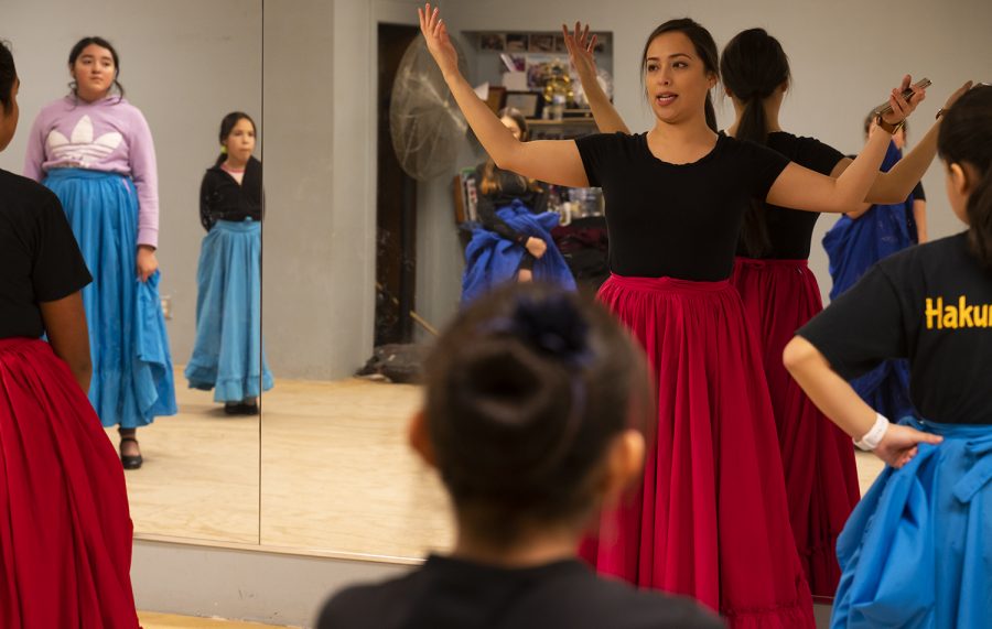 Artistic Director Blanca Acevedo walks junior dancers, dressed in blue and red practice skirts, through a choreography step for a dance originating in the Jalisco region of Mexico.