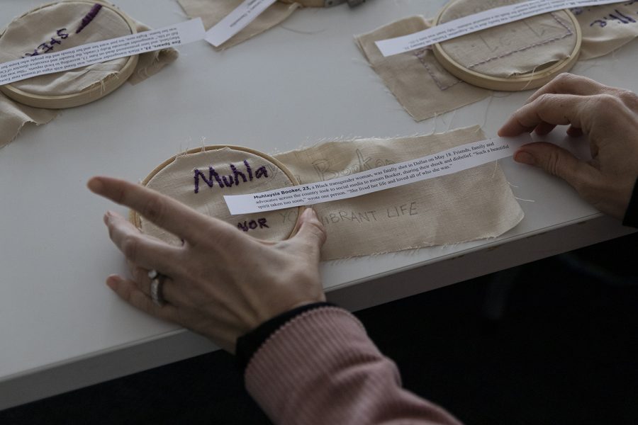 Colbey Reid, chair of the Fashion Studies Department, and other attendees are given the name and age of a transgender woman of color by quilter Melissa Blount to learn more about the circumstances in which they were killed, and to embroider their names and ages into the fabric for Blount’s quilt.