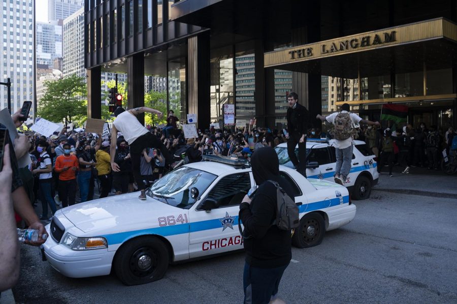 A group of protesters destroy a police vehicle, slashing its tires and jumping on the dash to shatter the glass.