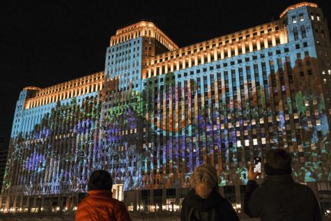 Onlookers gaze across the Chicago River off the corner of Wells Street and Wacker Drive as the Merchandise Mart is transformed into a vibrant coral reef through projections Saturday, April 9.