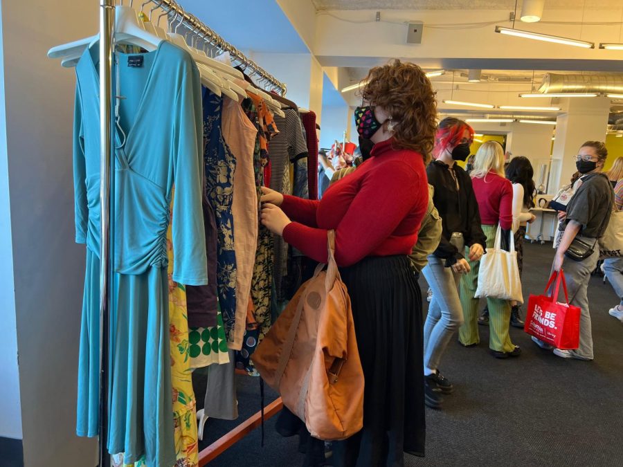 A Columbia student shuffles through donated clothes on a rack, playing part in the clothing swap event.