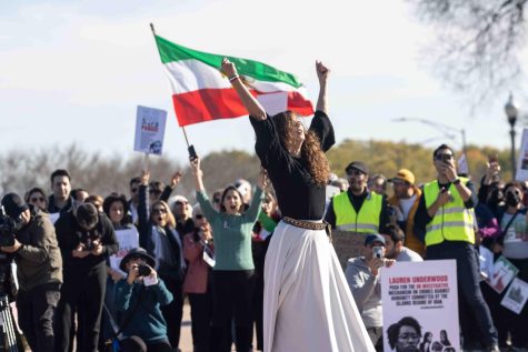 Surrounded by a crowd holding signs and cheering, a woman in the center of the protesters dances and raises her clenched fists to the sky. 