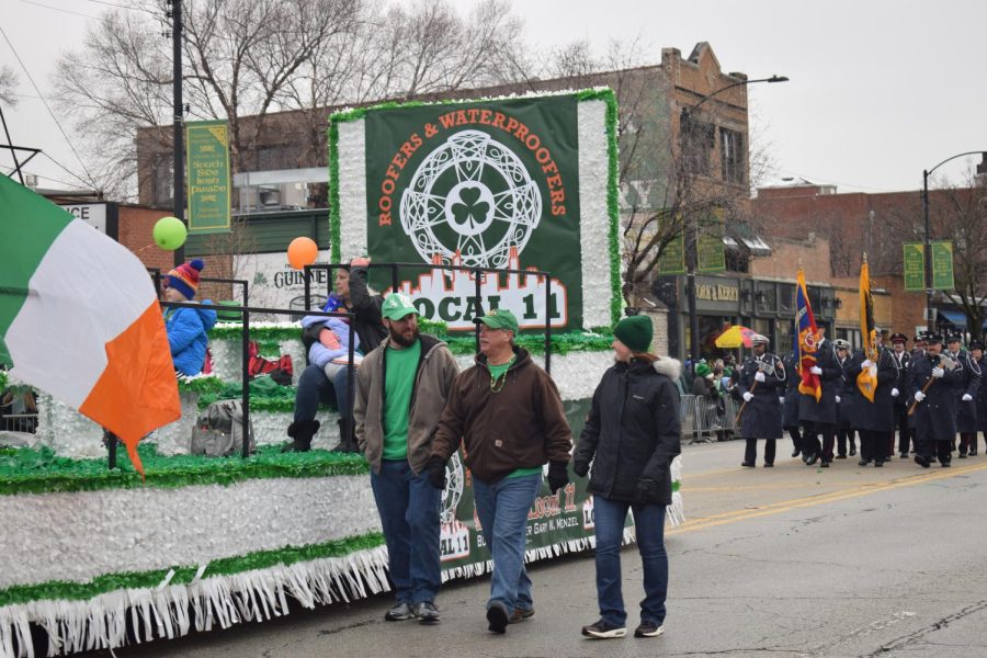 Three members of the Local 11 Union of Roofers, Waterproofers and Allied Workers walk alongside their float on Sunday, March 12. The Chicago Fire Department marches behind them.