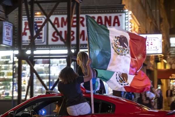 Two women ride out the window of a car while waving Mexican flags in the air and shouting Viva La Mexico on Saturday, Sept. 16, 2023.