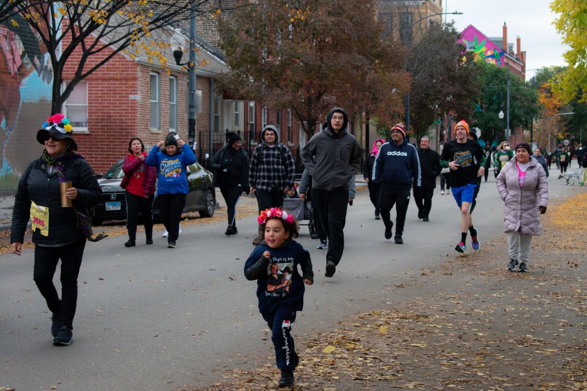 Una joven con una diadema floral llevaba una camisa que decia “Mi papi es mi ángel guardián”. Familias y amigos corren y caminan 5 kilómetros en la “Carrera de Los Muertos” de la Organización de Vecinos Unidos en el vecindario Pilsen de Chicago el sábado 28 de octubre de 2023.