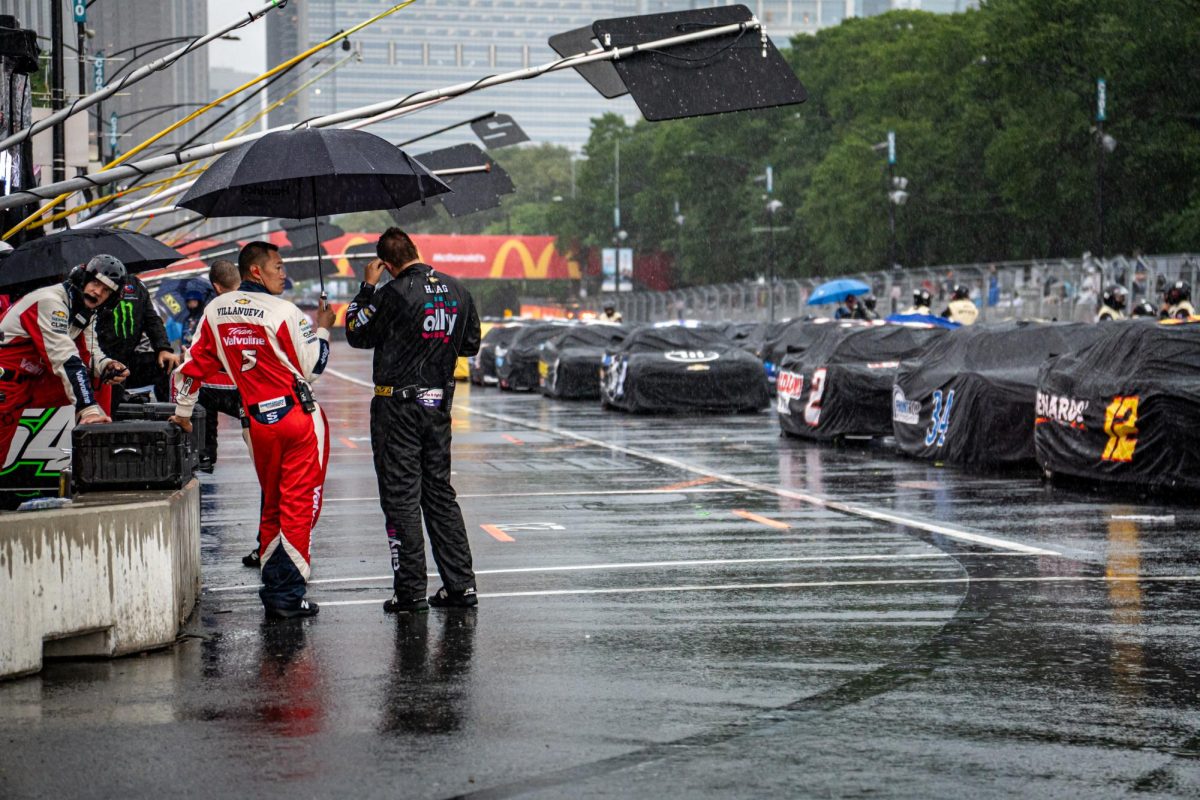 Pit crew members stand with umbrellas on pit road as they wait out the rain delays during the NASCAR Chicago Street Race on Sunday, July 7, 2024. A red flag was thrown, halting drivers from continuing temporarily. 