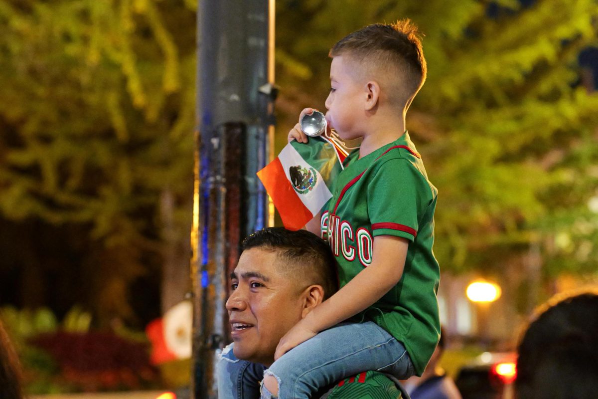 Un niño sentado en los hombros de su padre haciendo sonar un silbato en celebración del día de la independencia de México en la calle Michigan ave en Chicago el 14 de septiembre de 2024.