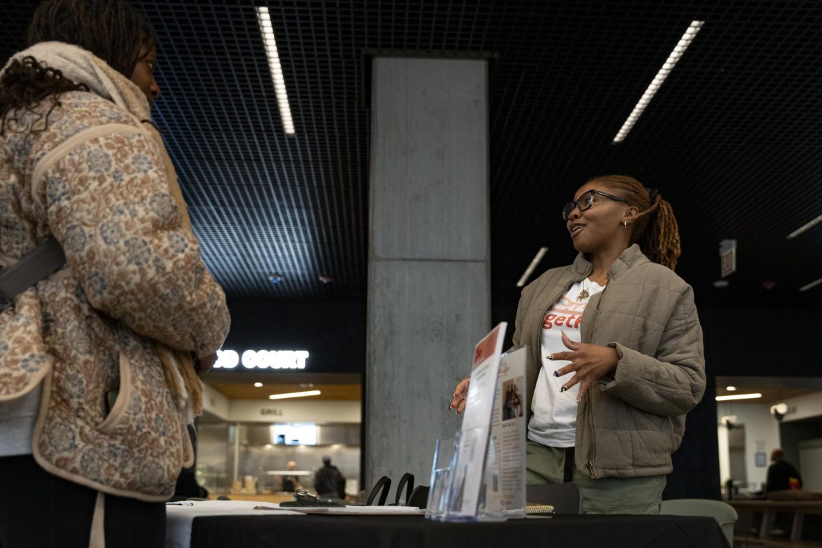 Sista Afya Community Organizer and Representative Kyndal Hill speaks to junior creative writing major Kayla Joseph about the organization’s program "Heal TogetHER" during the Wellness and Equity Fair on the first floor of the Student Center on Wednesday, Nov. 13, 2024. 