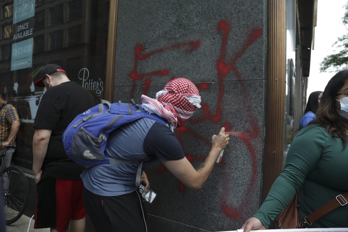 A protester vandalizing the facade of 2 E. Monroe St. during the "ICE Out" protest on Tuesday, June 10, 2025