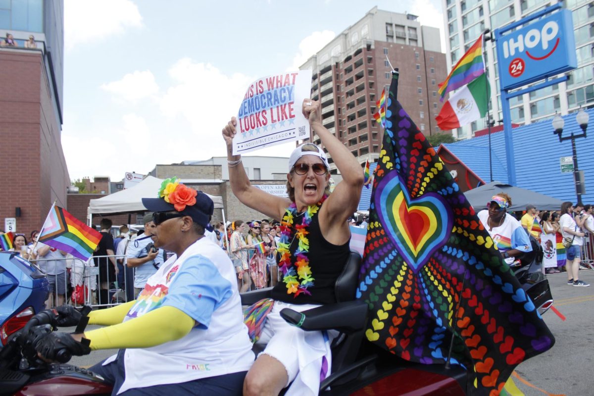 Parade participant, riding with the "Dykes on Bikes" motorcycle group, holds up a "This is what democracy looks like" sign while cheering with attendees at the Pride Parade on Sunday, June 29, 2025.