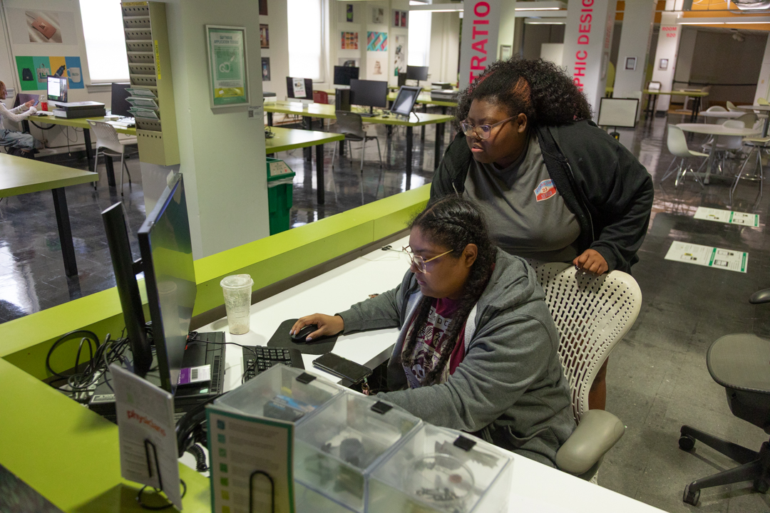 Junior animation major Neveah Wade and junior graphic design major Tysheah Gooden assist a student looking to check in and use the inkjet printers at the Digital Inkjet Printer Lab on the 9th floor of the 623 S. Wabash Ave. building on Tuesday, April 14, 2026. 