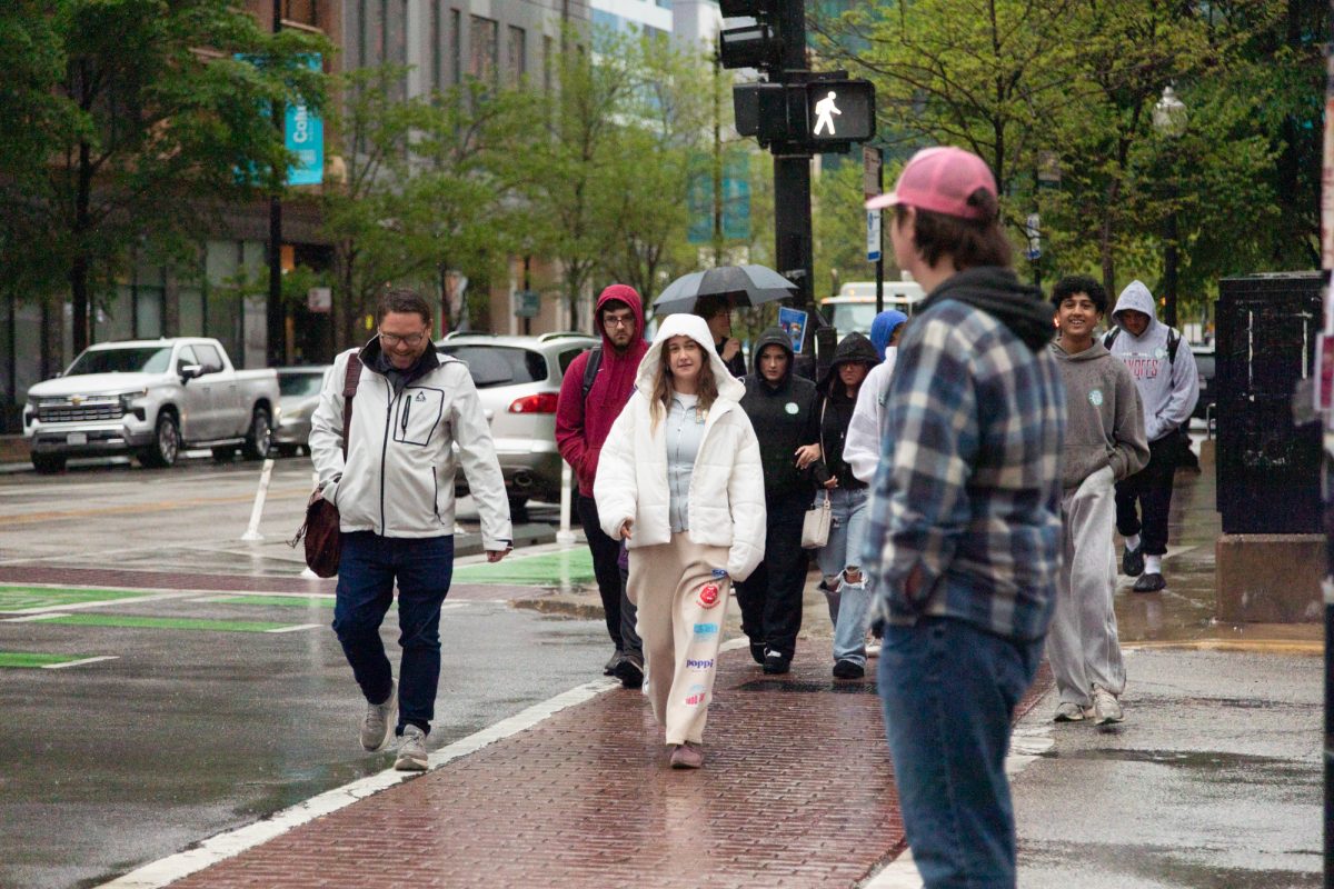 A group of parents and prospective students cross the street in the pouring rain to begin a tour of the Student Center on Monday, April 27, 2026.