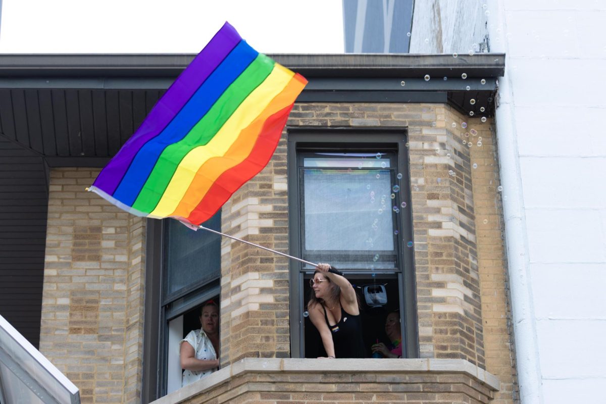 A resident waves a large rainbow flag from her apartment window as bubbles float past during the 55th annual Chicago Pride Parade on Sunday, June 28, 2026