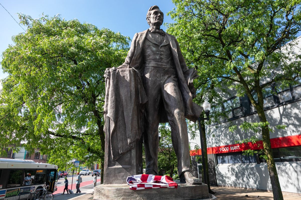 An American flag, folded and tucked at the feet of a statue of Abraham Lincoln in Lincoln Square following the massive storms in Chicago on Wednesday, June 17, 2026. This photo is part of The Columbia Chronicle's "77 Community Areas" project, documenting Chicago ahead of America's 250th birthday.