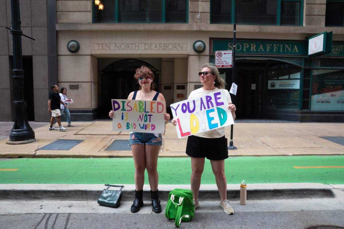 Two spectators hold handmade signs reading "Disabled is not a bad word" and "You are loved" along Dearborn Street during the Disability Pride Parade in Chicago on Saturday, July 25, 2026.