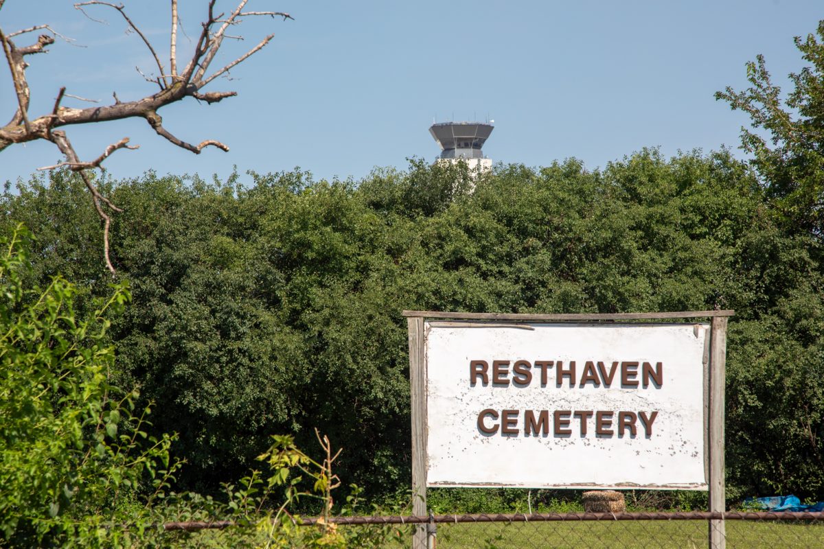 A control tower at the O’Hare International Airport looks over Resthaven Cemetery, situated in the middle of O’Hare airport, on Tuesday, July 14, 2026. The cemetery remains untouched while St. Johannes Cemetery was relocated, and a runway was consequently built on top of it. It was a grave undertaking for the city to ensure a respectful relocation of a burial site that had nearly 1,500 graves in 2013. This photo is part of the Columbia Chronicle’s “77 Community Areas” project, documenting Chicago in celebration of America’s 250th birthday.