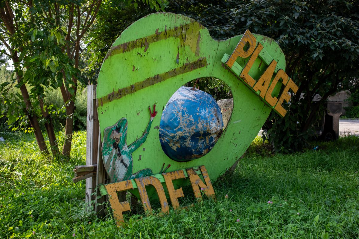 A fallen sign, denoting 'Eden Place' with a wooden frog and globe, sits on the ground in what once was a community gathering space and sanctuary of the same name in Fuller Park on Wednesday, Aug. 19, 2026. Before the land was developed, it was an illegal dumping grounds for waste and construction debris. It was then cleaned up and developed for farming purposes. This photo is part of the Columbia Chronicle’s “77 Community Areas” project, documenting Chicago in celebration of America’s 250th birthday. 