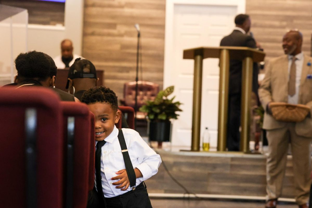 Jayse Stapleton hides behind church pews during a service in Chicago's Burnside neighborhood, on Sunday Sept. 6, 2026. At the small corner store Burnside church, New Covenant Harvest Church, celebrates Jayse’s fourth birthday with his family and congregation. This photo is part of the Columbia Chronicle’s “77 Community Areas” project, documenting Chicago in celebration of America’s 250th birthday.