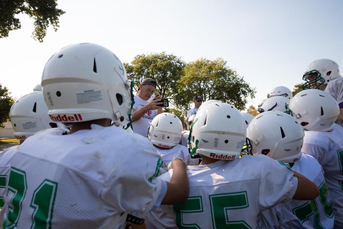 Assistant coach Brad Czachor uses a smartphone to go over plays with St. Juliana Trojan players during practice at Oscar Brooks Park in the Edison Park neighborhood on Friday, Sept. 11, 2026. This photo is part of the Columbia Chronicle’s “77 Community Areas” project, documenting Chicago in celebration of America’s 250th birthday.