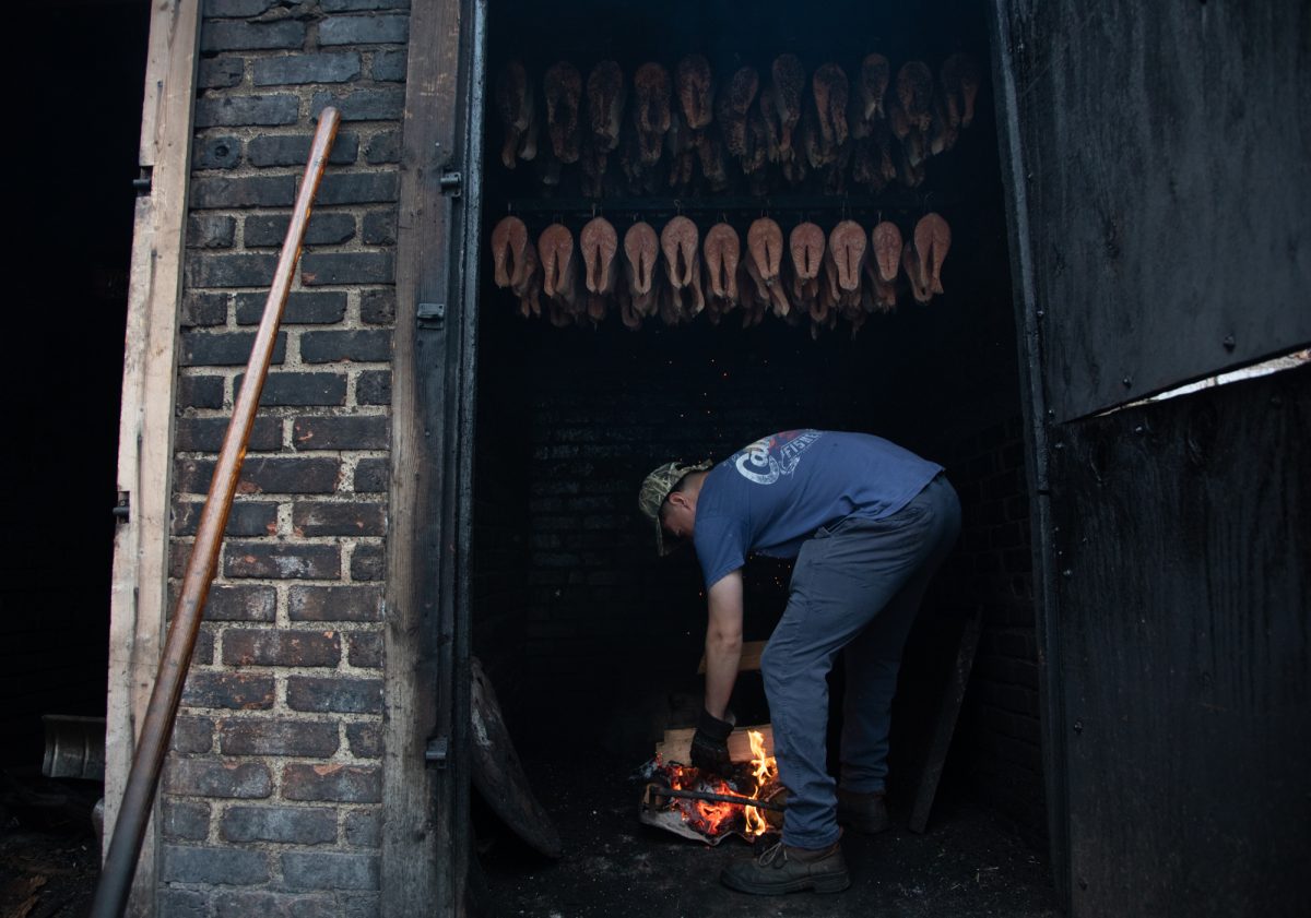 Giovanni Rosas stokes the fire with cherry and oak wood for the signature smoked salmon and pepper & garlic salmon at Calumet Fisheries in South Chicago on Tuesday, Sept. 1, 2026. This photo is part of the Columbia Chronicle’s “77 Community Areas” project, documenting Chicago in celebration of America’s 250th birthday.