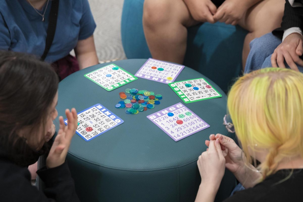 Students gather around a low table with bingo cards and marker chips during a Grocery Bingo event to win groceries at the Hive in the 618 S. Michigan Ave. building on Tuesday, Oct. 6, 2026.