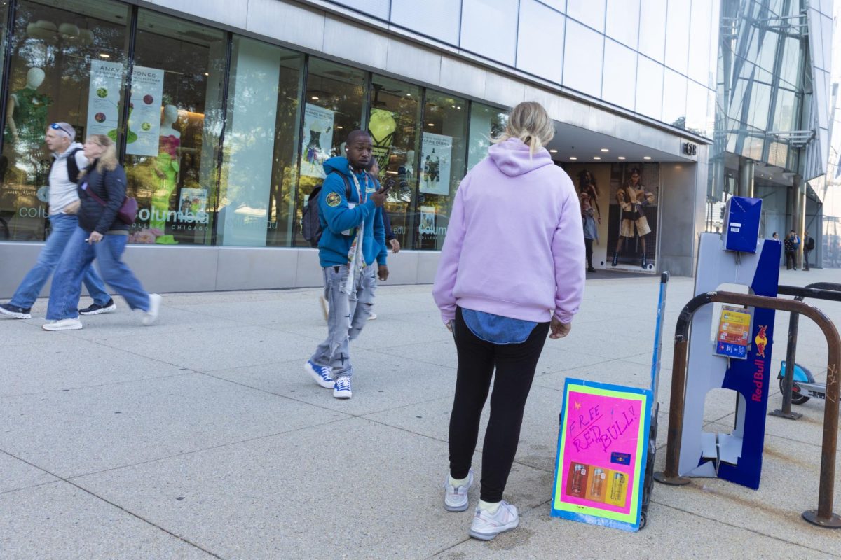 Red Bull brand ambassador Jessica Mikos distributes free energy drinks from a promotional display with handwritten signs on the sidewalk outside of the 618 S. Michigan Ave. building on Monday, Oct. 5, 2026.