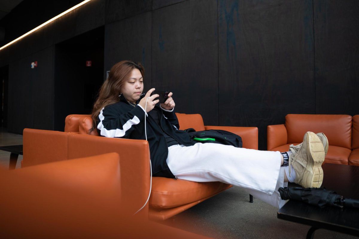 Senior graphic design major Trixie Tran rests her feet on a coffee table while using their phone in the Student Center on Friday, Oct. 16, 2026.
