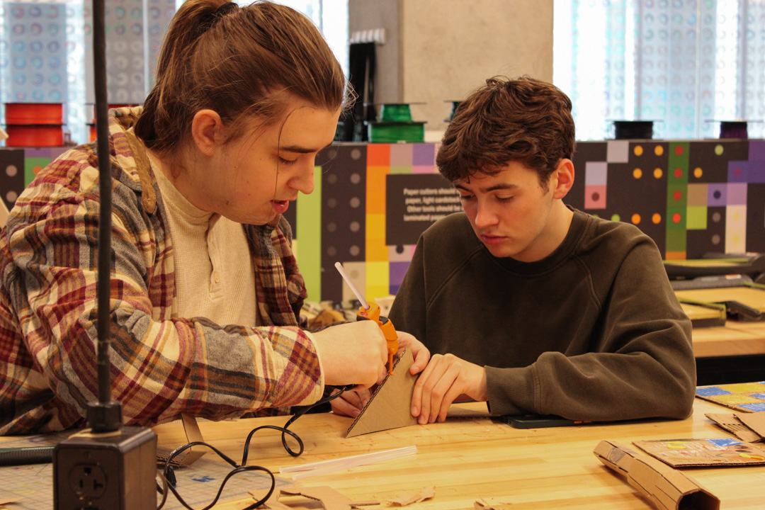 Mac McCarter, a sophomore music production major, holds two pieces of cardboard in place while Isaac Feryance, a junior animation major, applies hot glue in the Makerspace on the second floor of the Student Center on Friday, Oct. 2, 2026.